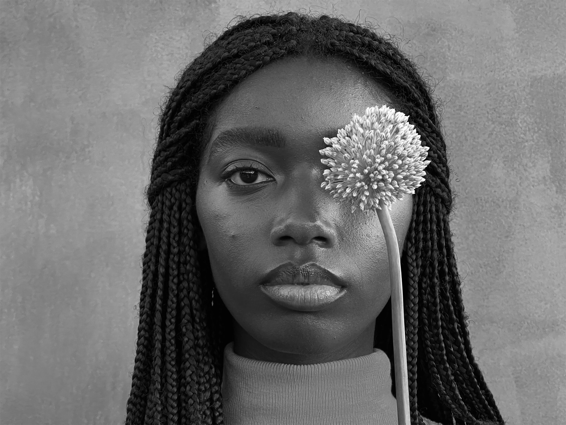 Caméra grand angle iPhone 13 Pro Max Photo en noire et blanc du visage d'une femme regardant droit dans l'objectif avec un pissenlit recouvrant son œil gauche